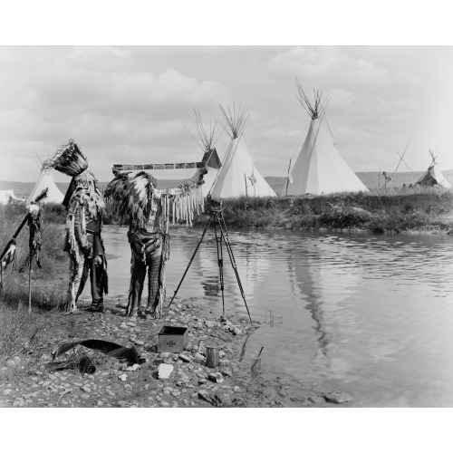 Two Native Americans, Wearing Feather Headdresses, Looking At Photographic Film; They Stand Next...