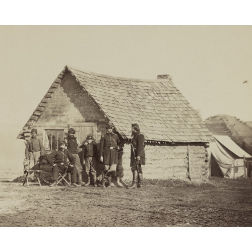 A Group Of Soldiers, And Two Young Men, One An African American, Stand Outside Of Log Cabin...